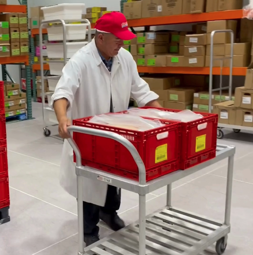 Meat factory employee pushes a cart of Tosca meat crates while trialing Meat RPCs as part of the tosca pilot program.